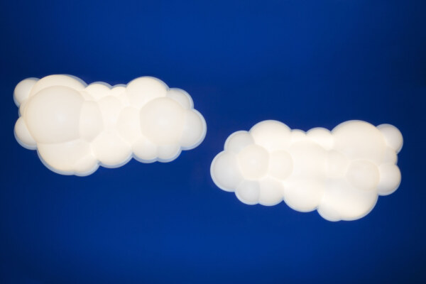 Zwei wolkenförmige Wandleuchten vor einem tiefblauen Hintergrund, die ein gleichmässiges und warmes Licht ausstrahlen und einen kontrastreichen, modernen Look erzeugen.