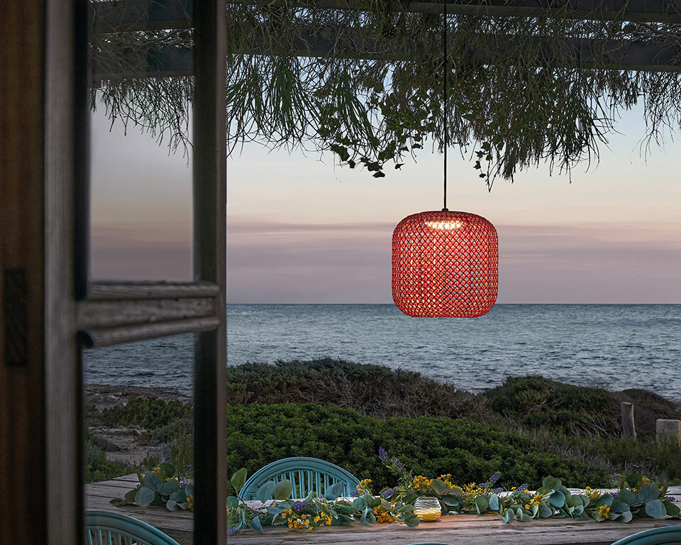 Eine zylindrische Hängeleuchte mit einem durchbrochenen, gemusterten Schirm, an einem schlanken Kabel befestigt.