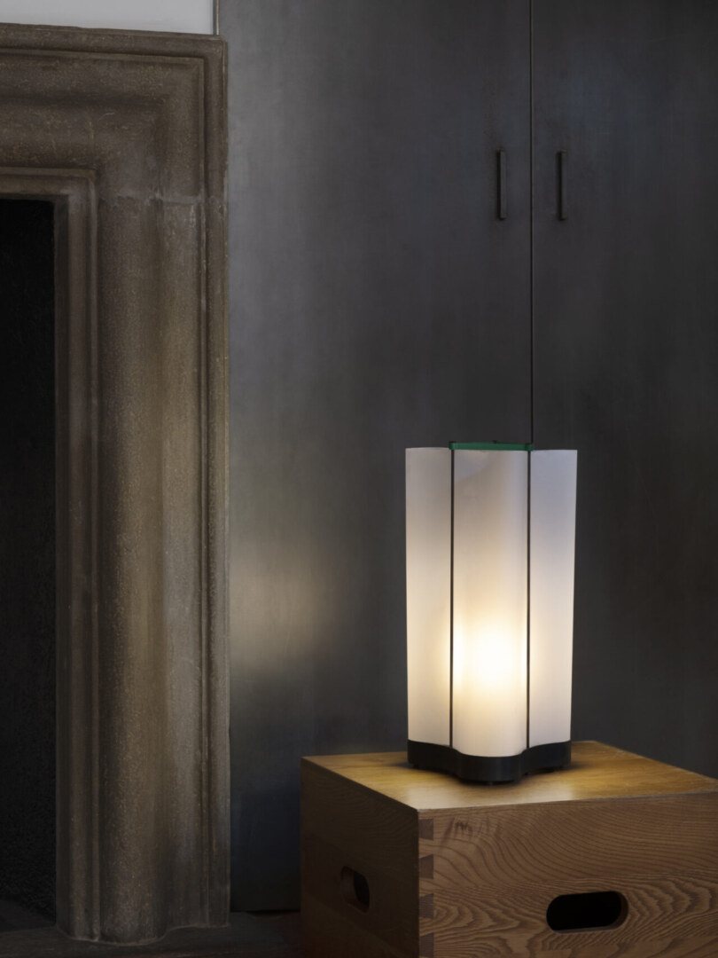 Das Bild zeigt eine schlanke, moderne Stehlampe mit einer rechteckigen Form. Der untere Teil des Lampensockels ist dunkel, während der obere Teil aus durchscheinendem Material gefertigt ist, das sanftes Licht ausstrahlt. Das minimalistische Design der Lampe passt gut in ein modernes Interieur.