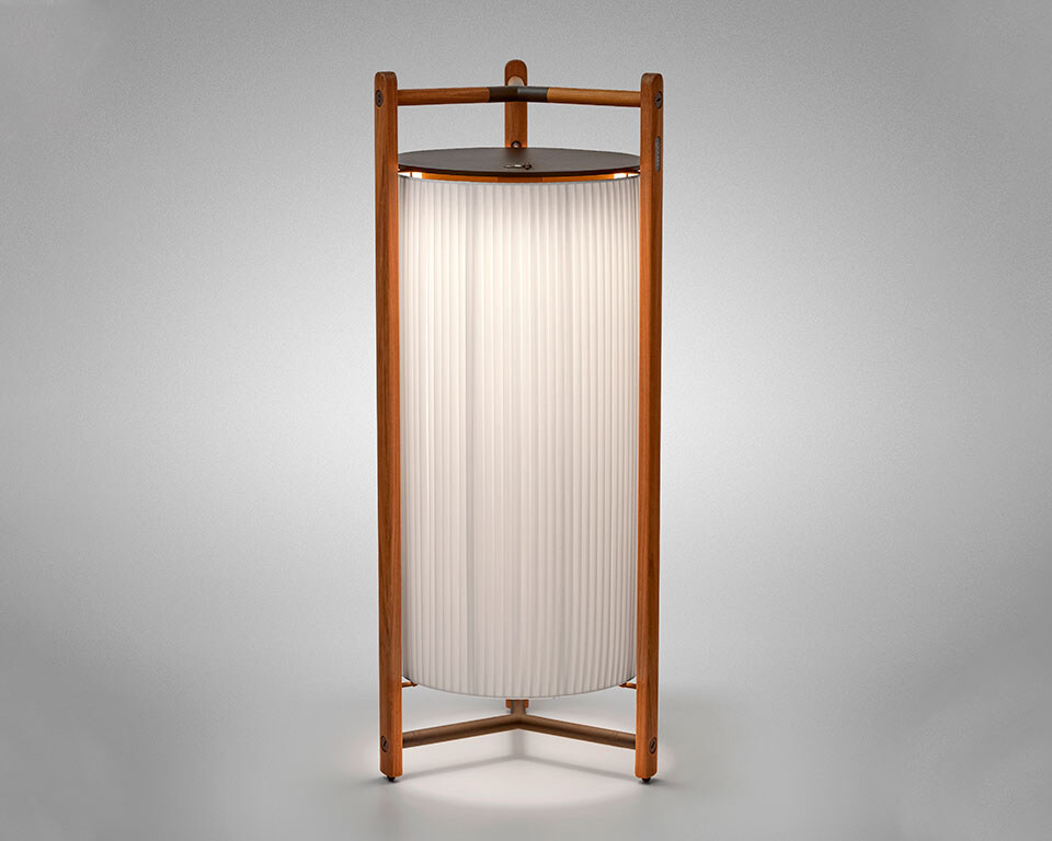 Kando-P111R-white_1 Eine moderne Tischlampe mit einer zylindrischen, geriffelten Schirmstruktur, umgeben von einem robusten dreibeinigen Rahmen aus Holz, der oben einen integrierten Griff aufweist. Die Lampe strahlt weiches Licht nach unten aus.