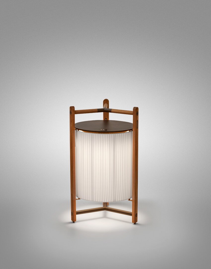 Kando P76R (1) Eine moderne Tischlampe mit einer zylindrischen, geriffelten Schirmstruktur, umgeben von einem robusten dreibeinigen Rahmen aus Holz, der oben einen integrierten Griff aufweist. Die Lampe strahlt weiches Licht nach unten aus.