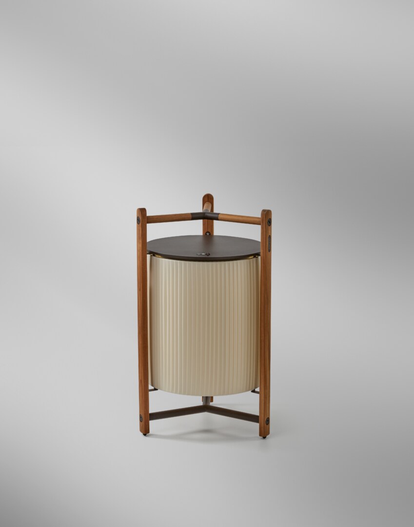 Kando P76R (4) Eine moderne Tischlampe mit einer zylindrischen, geriffelten Schirmstruktur, umgeben von einem robusten dreibeinigen Rahmen aus Holz, der oben einen integrierten Griff aufweist. Die Lampe strahlt weiches Licht nach unten aus.