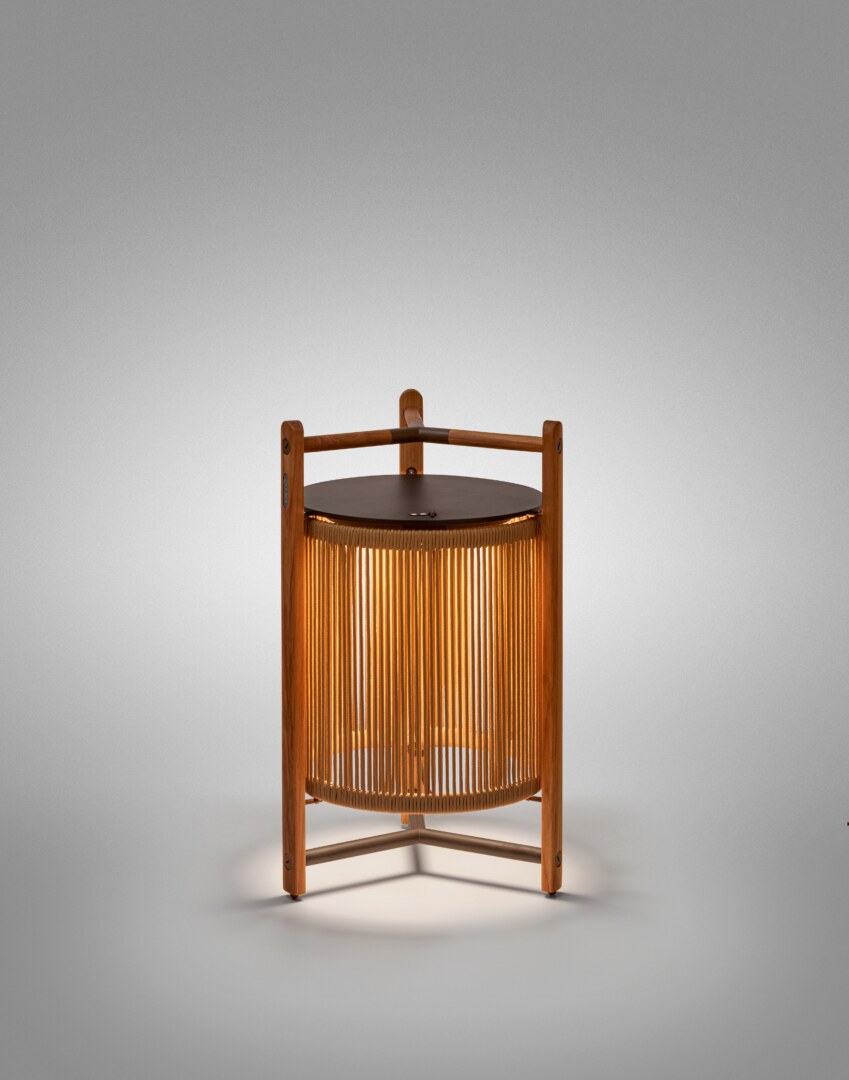 Kando P76R Outdoor (2) Eine moderne Tischlampe mit einer zylindrischen, geriffelten Schirmstruktur, umgeben von einem robusten dreibeinigen Rahmen aus Holz, der oben einen integrierten Griff aufweist. Die Lampe strahlt weiches Licht nach unten aus.