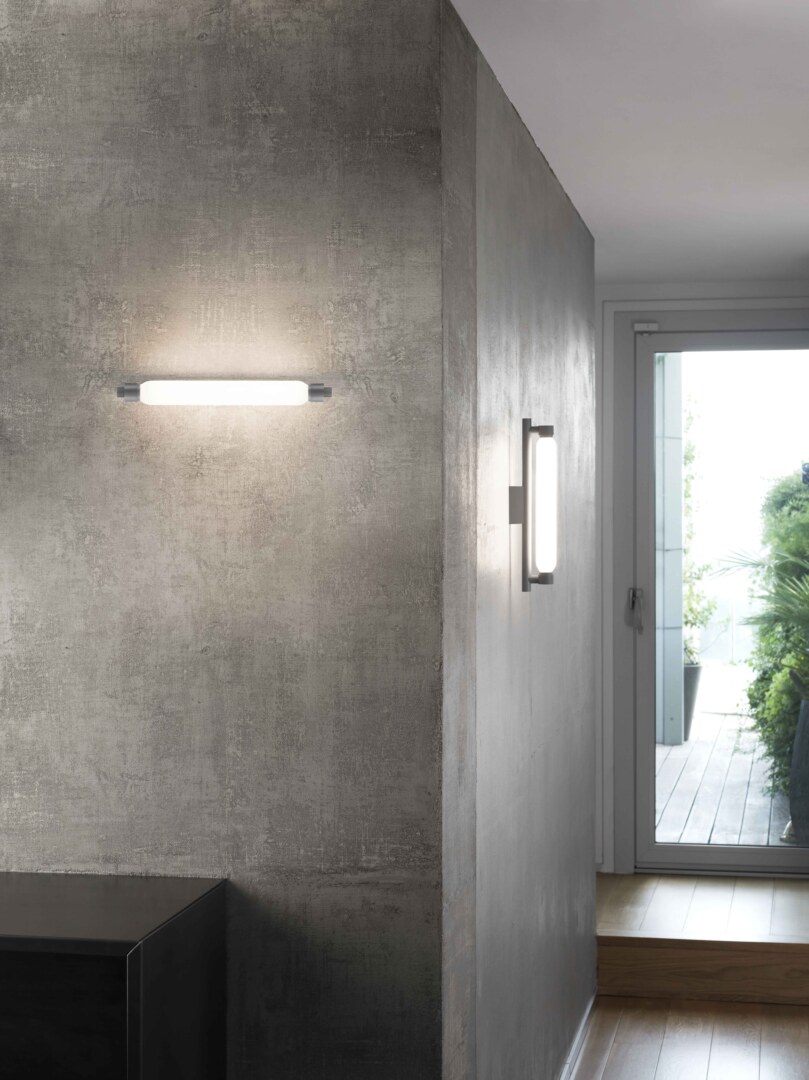Moderne Wandleuchte La Roche in Grau, montiert an einer Betonwand, mit diffusem, warmem Licht, das eine elegante und stilvolle Atmosphäre schafft.