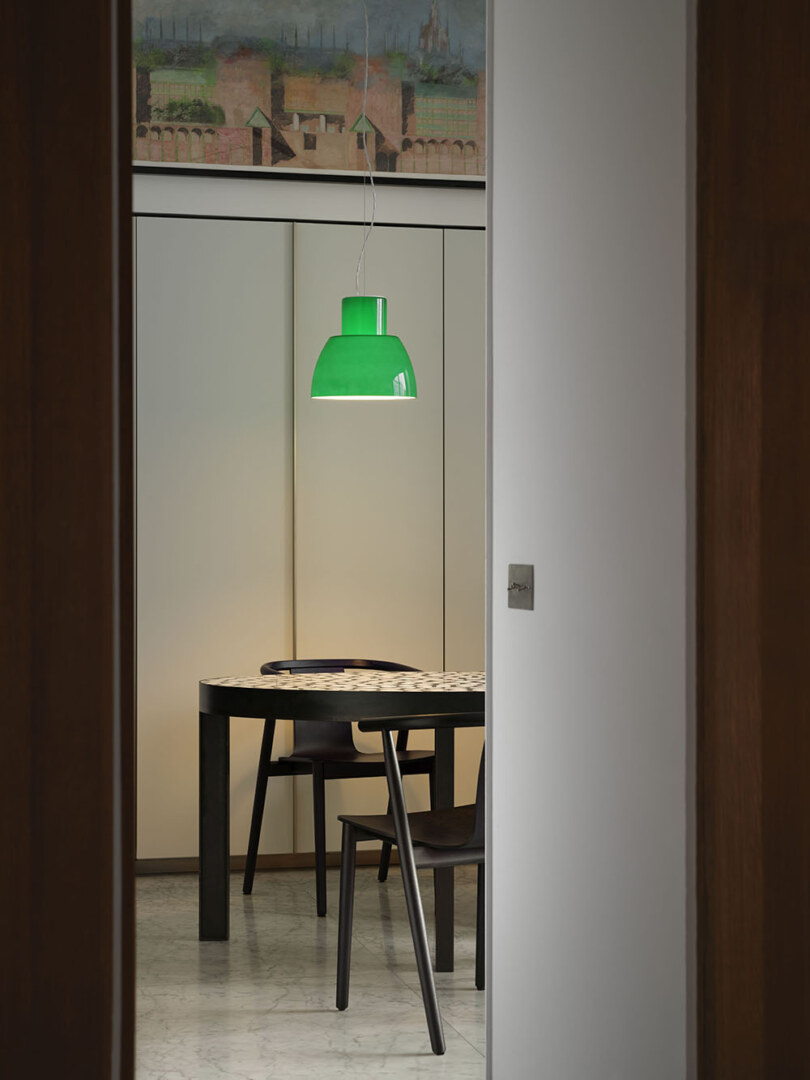 Eine grüne Pendelleuchte hängt über einem runden Esstisch in einem modern eingerichteten Raum.