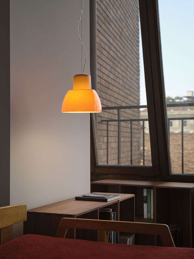 Eine orangefarbene Pendelleuchte hängt in einem gemütlichen Raum mit grossen Fenstern und einem Schreibtisch.