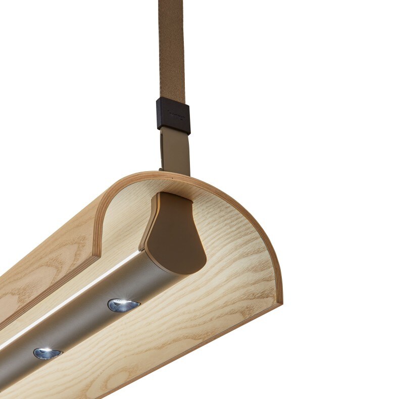 aluet-s100_Pendelleuchte_Details Eine moderne Pendelleuchte mit einer langen, horizontalen Holzleiste, an deren Enden schwarze Metallelemente befestigt sind. Die Leuchte wird von zwei dünnen, schwarzen Kabeln gehalten, die sowohl als Aufhängung dienen als auch die elektrischen Verbindungen beinhalten. Das warme Licht der Leuchte wird durch röhrenförmige Lampen erzeugt, die unter der Holzleiste angebracht sind.